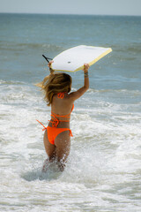 A girl running into the ocean with a boogie board 
