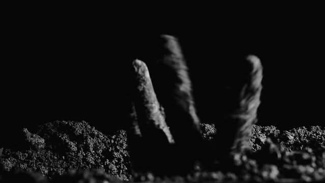 A zombie hand covered in earth climbs out of a grave. At night, a dead man's hand rises from under the ground. An epidemic. Close-up. Black and white video