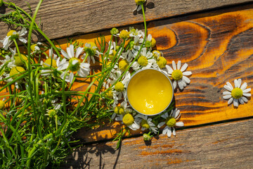 Pharmacy chamomile flowers and chamomile ointment. A jar with cream, balm, chamomile flowers on a wooden background. cosmetic creams, lip balm with flowers on a wooden table. Selective focus.