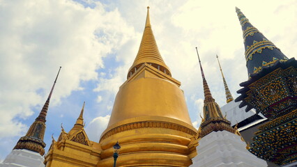 Fototapeta premium herrlicher Tempel Wat Phra Kaeo in Bangkok mit Stupas, goldener Pagode unter blauem Himmel mit Wolken