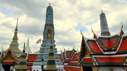 Fototapeta premium herrlicher Tempel Wat Phra Kaeo in Bangkok mit Stupas und roten Dächern unter blauem Himmel mit Wolken