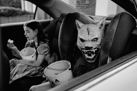 Two children (brother & sister) dressed up for Halloween in the car ready to go trick or treating in Australia. One child wears a werewolf mask, the other child is dressed up as a vampire princess