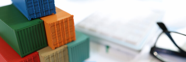 Several colorful cargo containers with us dollar bills and glasses on financial reports.