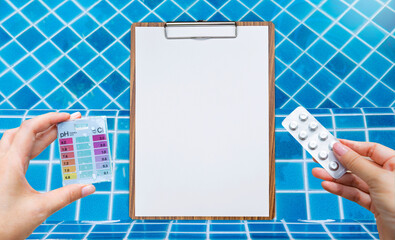 Pool tester test kit and reagent tablets in girl hand with wooden clipboard over swimming pool...
