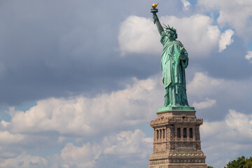 Obraz premium Iconic representation of freedom and independence, the Statue of Liberty with flaming torch on Liberty Island. The Lady on a Pedestal is surrounded by clouds. City landmark. American history.