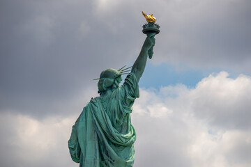 Fototapeta premium A close up on an iconic representation of freedom and independence, the Statue of Liberty with flaming torch on Liberty Island. The Lady on a Pedestal is surrounded by clouds. American history.
