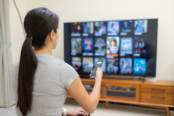 Woman watch TV and use remote control for choosing program at home