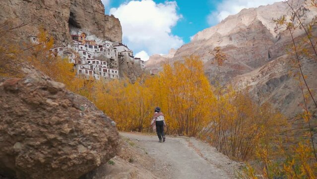 Rear view of tourist woman walking towards ancient Phugtal monastery during autumn season at Zanskar, Ladakh, India. Buddhist Monastery in cave.  Indian young woman on vacation.