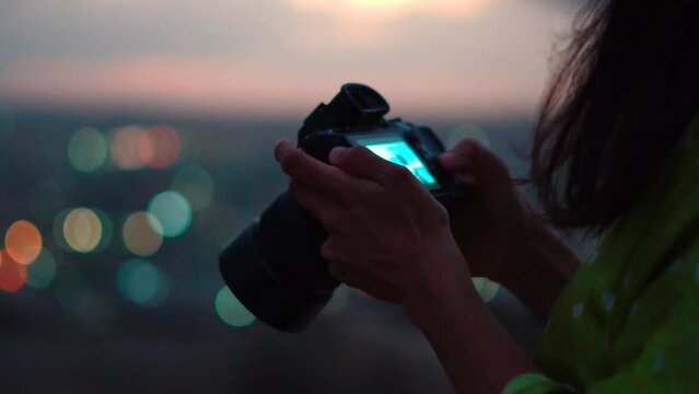 Close up shot of camera in female hands. Girl reviewing images after photoshoot. Closeup of camera with bokeh lights in background.
