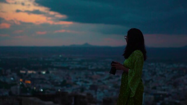 Silhouette shot of young Indian woman holding camera while looking at Bhuj city in Kutch, Gujarat. Female photographer shooting during late evening. Travel and holidays concept.