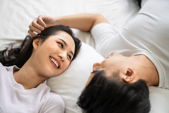 Asian new marriage couple lying down on bed and looking at each other. 