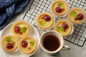 fruit pie on a cooling rack and a cup of tea. delicious and healthy dishes. there are kiwi chunks, grapes, and raisins. on a white marble table.