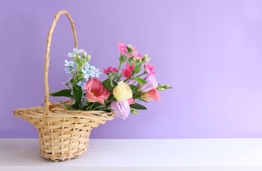 Fototapeta na wymiar image of delicate pink flowers in the wicker basket over wooden table and purple background