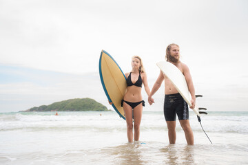 Couple of surfers holding hands and looking at each other on beach