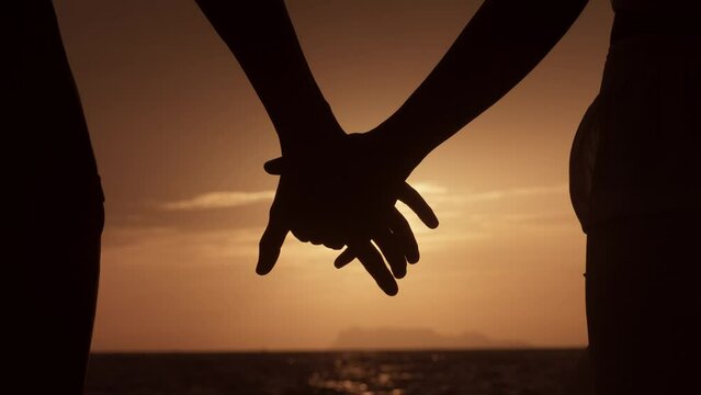 Close up silhouette man and woman touching hands together at sunset beach. Romantic couple couple holding each other hand's enjoying romantic date. Love couple holding hands on sea sunset background.