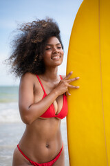 Portrait of smiling young woman in bikini with surfboard at beach
