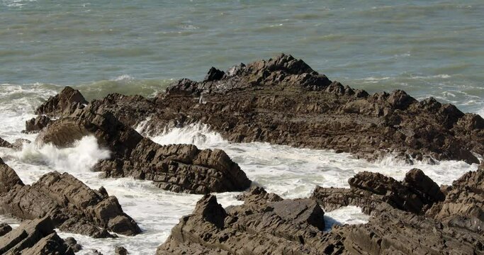 Wide shot of sea breaking over jagged sedimentary rocks in the Cornish sea at Hartland Quay, Stoke, Hartland, Bideford