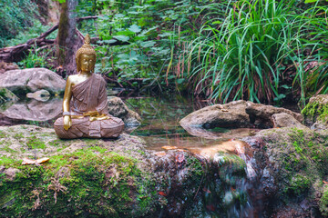 Buddha statue sitting in a mountain river meditating on a waterfall