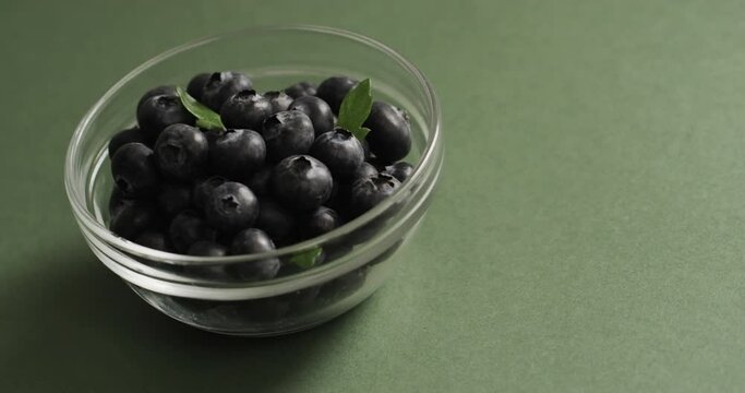 Micro video of close up of bowl with blueberries with copy space on green background