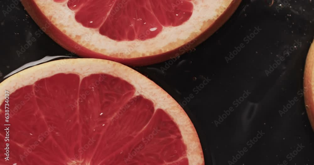 Poster micro video of close up of slices of red grapefruit with copy space on black background