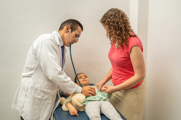 doctor examining child stomach with stethoscope. Pediatrician checking on girl belly at hospital or...