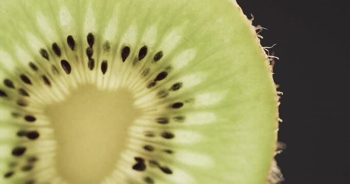 Micro video of close up of slice of kiwi fruit with copy space on black background