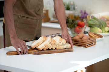 Slices of bread arranged on a wooden tray on a white table, man puts a tray of bread on the table ready to serve, close up