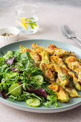 Fried zucchini flowers in batter and mix salad with cucumbers close up