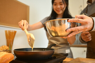 Smiling young woman pouring pancake batter onto a hot electric griddle, couple preparing breakfast together