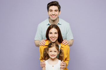 Young happy parents mom dad with child kid daughter girl 6 years old wear blue yellow casual clothes stand behind each other posing look camera isolated on plain purple background. Family day concept.