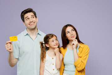 Young parents mom dad with child kid daughter girl 6 year old wear blue yellow casual clothes hold mock up credit bank card look aside on area isolated on plain purple background Family day concept