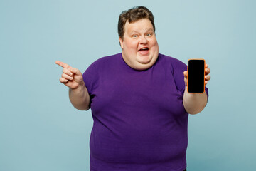 Young surprised amazed chubby overweight man wear purple t-shirt casual clothes hold use mobile...