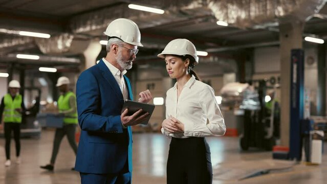Guy Supervisor Talking and Using Tablet with Lady Manager while Standing Together at Warehouse. Visitor or Customer Visiting to Look at Stock and Plant Before the Acquisition of Factory Company