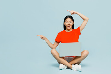 Full body young IT latin woman wear orange red t-shirt casual clothes sitting hold use work on...