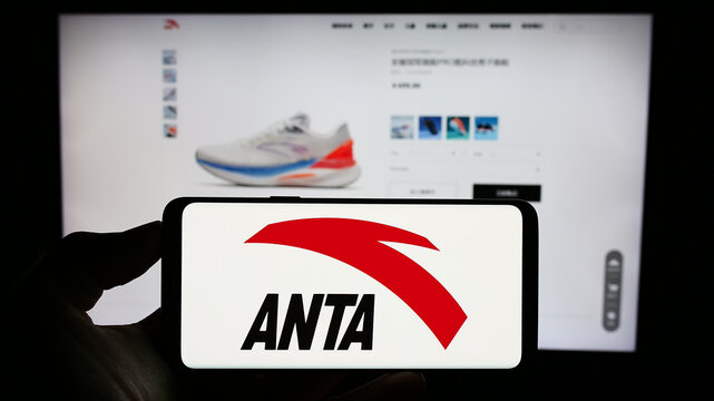 Stuttgart, Germany - 08-15-2023: Person holding cellphone with logo of Chinese company Anta Sports Products Limited on screen in front of webpage. Focus on phone display.