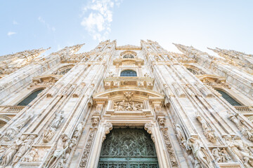 Milan Cathedral, Italian: Duomo di Milano, or Metropolitan Cathedral-Basilica of the Nativity of Saint Mary. View of main door and white marble facade on sunny summer day. Milan, Lombardy, Italy