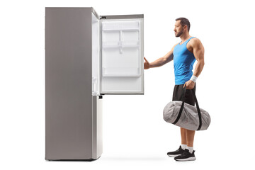 Fit man holding a sports bag and opening an empty fridge