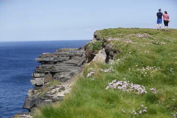 Fototapeta na wymiar Cliffs at Downpatrick Head in the West of Ireland in County Mayo. A couple standing at the edge of the cliffs, watching the ocean.