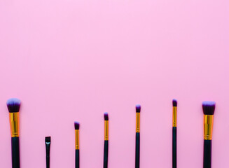 set makeup brushes on pink colored background with copy space. Top view.