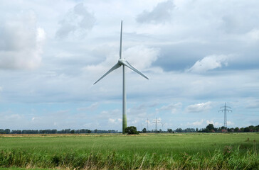 Windenergie: Ein riesiges Windrad in einer ländlichen Gegend mit bewölktem Himmel und mehreren...