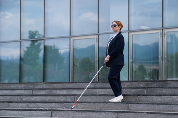 Blind business woman descending stairs with a tactile cane from a business center.