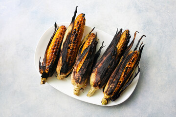 Grilled corn cobs on a white plate.
