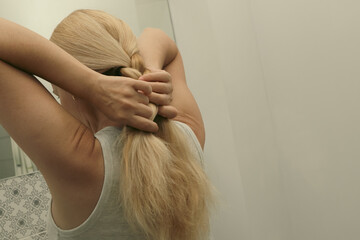 Blonde woman braiding her hair, close up photo. Hair Braid. Rear view closeup. Woman tied her in braid at home