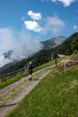 Fototapeta na wymiar trekking man walking up gravel road on forest covered mountain to a malga, mountain hut, with alpine restaurant in Italian dolomites with low clouds 