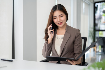 A gorgeous Asian businesswoman is reading some details on a document while talking on the phone