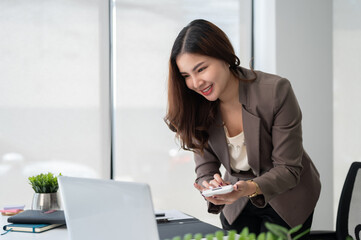 A beautiful Asian businesswoman bending over a table and using a calculator, working in the office.