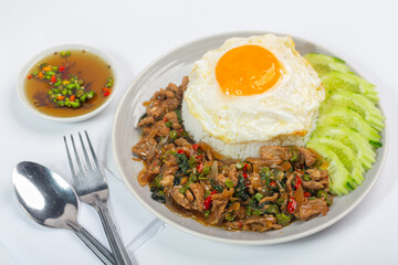 Stir-fried beef with basil leaves, fried egg and cucumber slices on white background