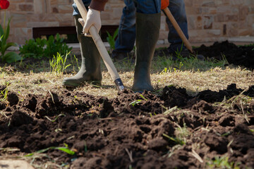 Two people are digging earthen plot in front of  house..