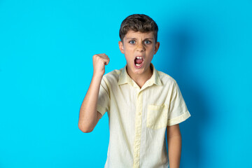 Beautiful kid boy wearing casual shirt angry and mad raising fist frustrated and furious while...