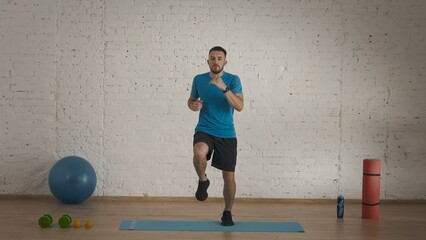 Man fitness trainer in sportswear doing running and jumps in place warm up for online class at the...